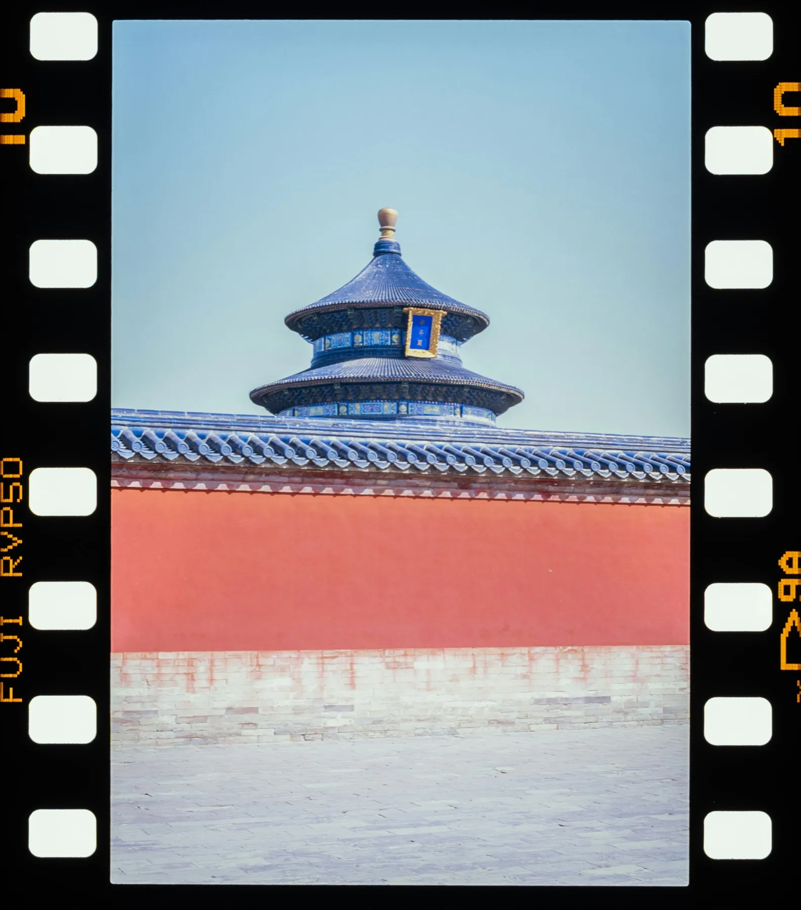 The blue-tiled roof of the Temple of Heaven above a red wall in Beijing, scanned from Fuji slide film with the sprocket border visible